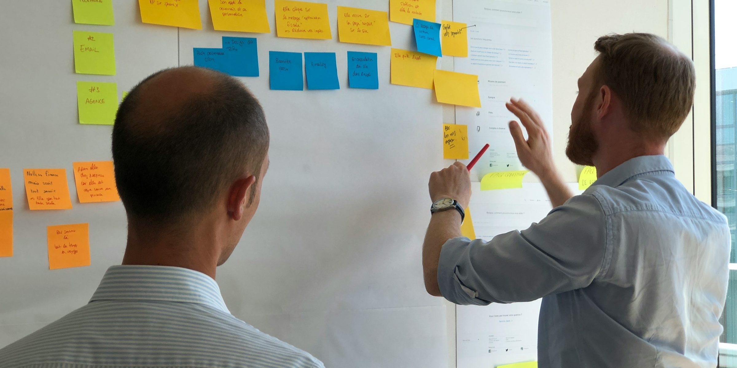 Two people working through a wall of sticky notes in a workshop