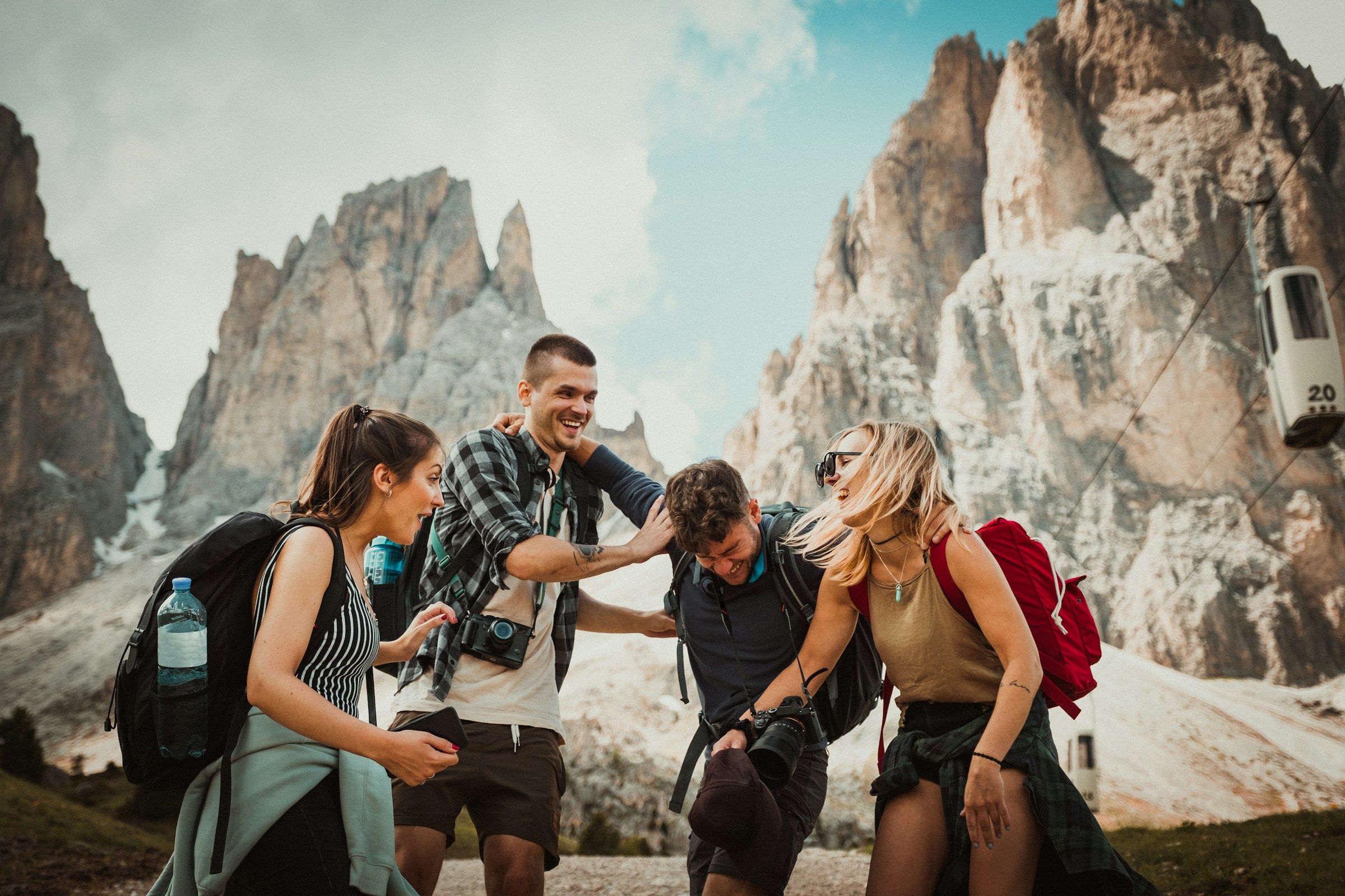 Four friends laughing together on a mountain trail, packs on their backs