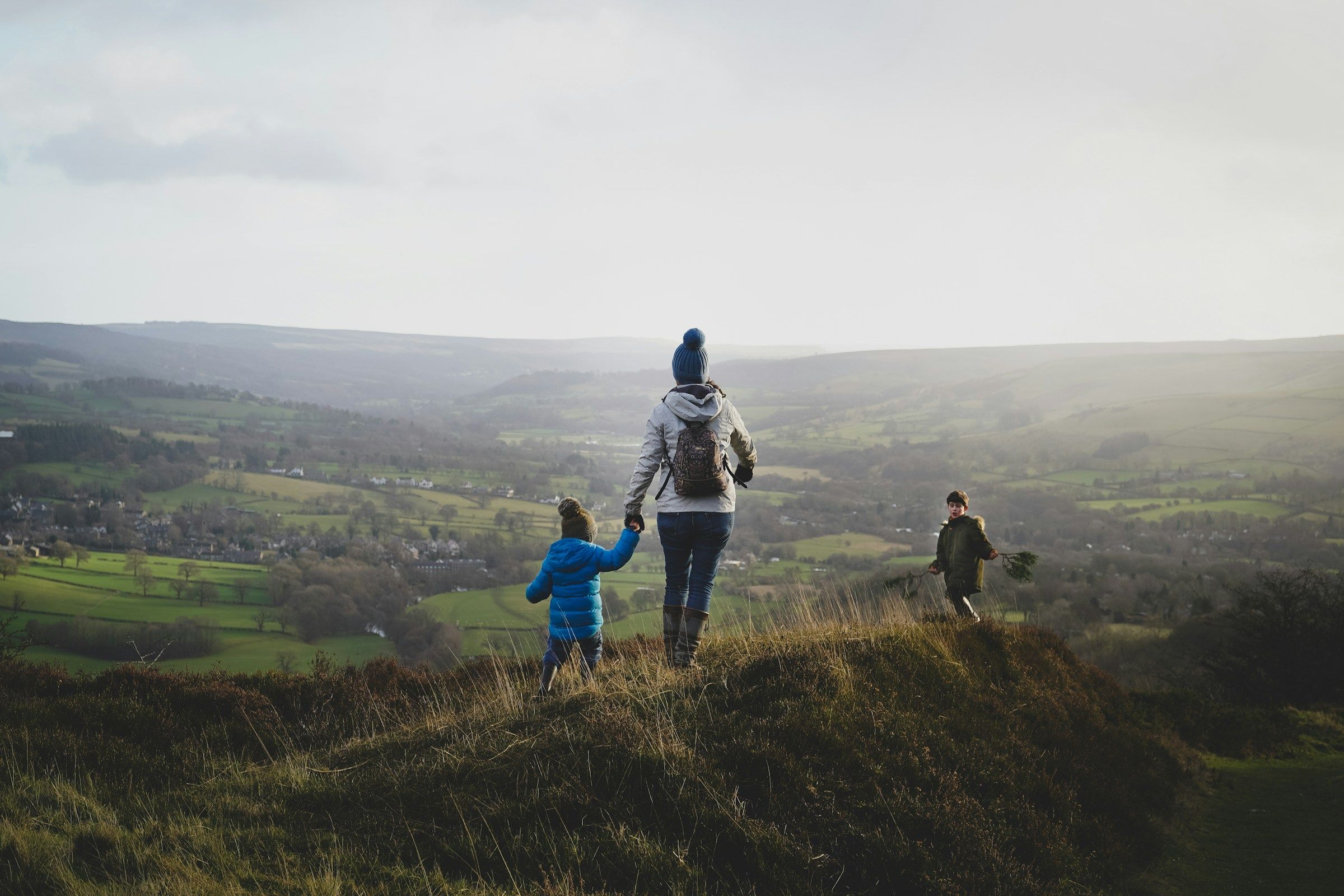 A parent and a small child walk hand in hand along a hilltop while another child runs ahead