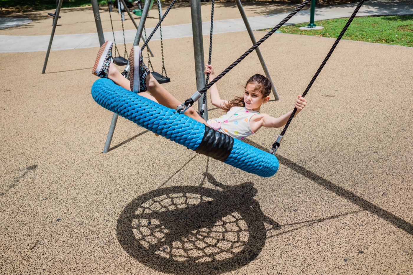 A child mid-swing on a playground, long shadow on the ground