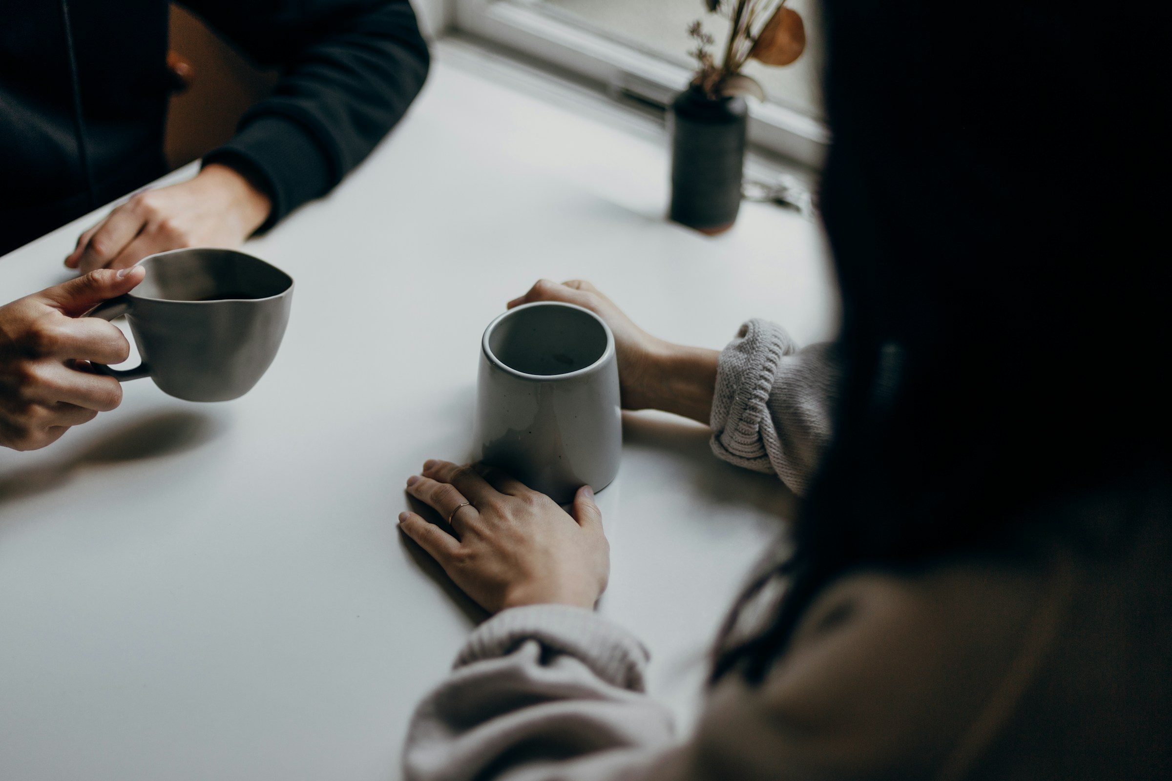 Two people talking across a table with coffee mugs