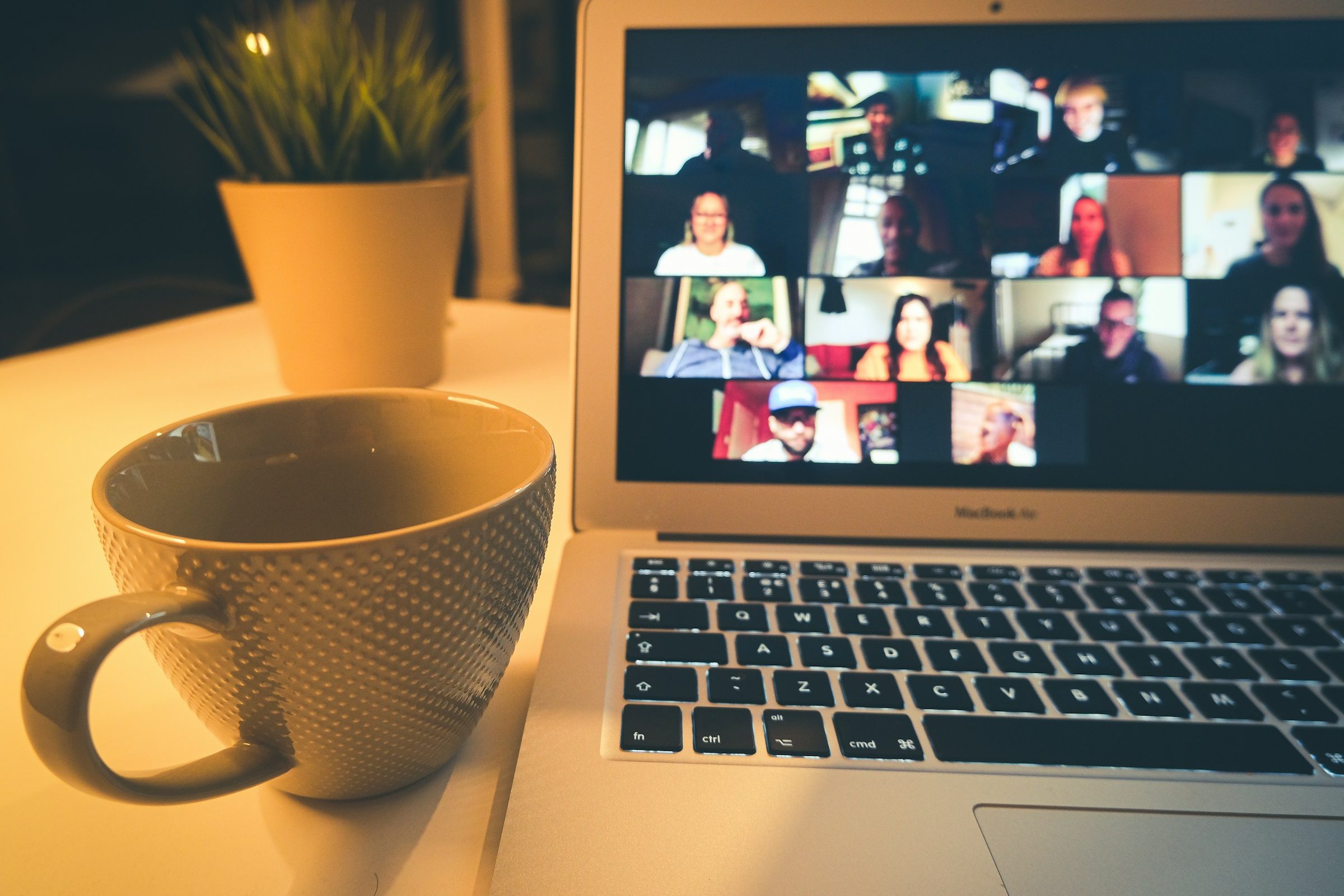 A laptop showing a video call with many people, beside a coffee mug