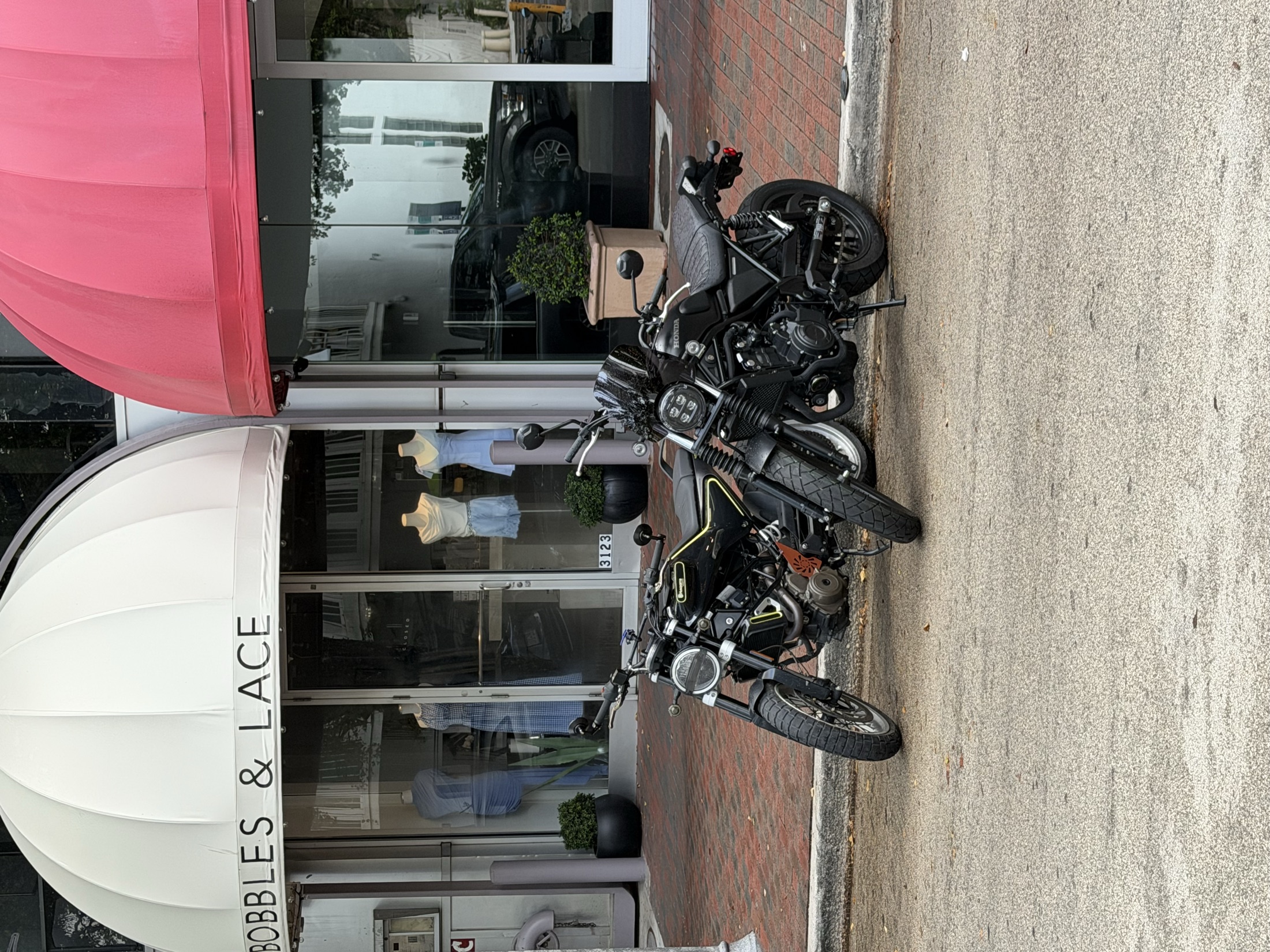 Two motorcycles parked outside a boutique with white and red awnings